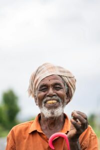 Elderly farmer smiling broadly, holding crops in a field. Rural lifestyle portrait emphasizing joy and tradition.